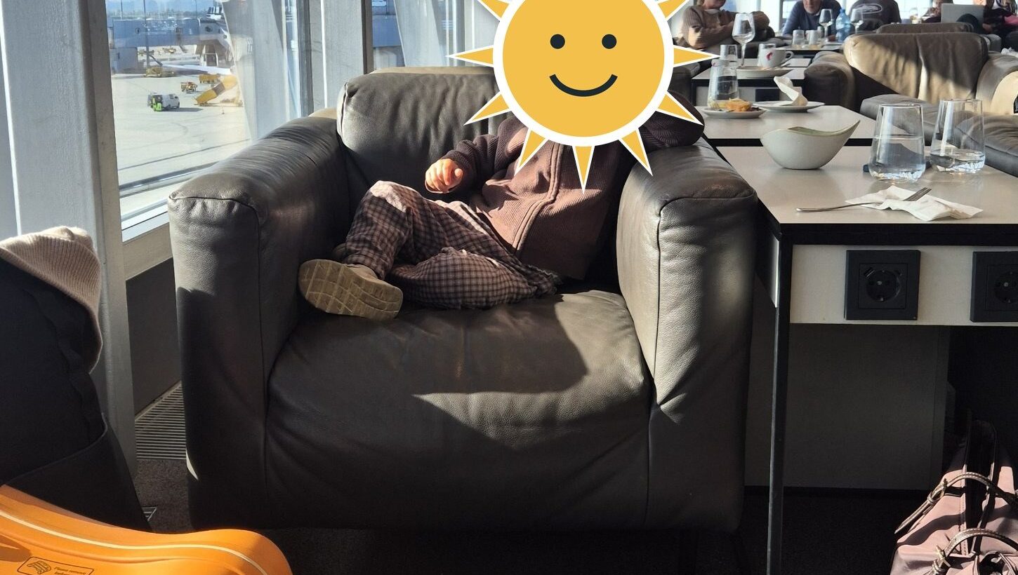 Finn im Lounge-Sessel am Flughafen Wien, davor sein Kinderkoffer im Tiger-Look